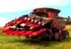 A large red harvester with front attachments sits in a field, showcasing the latest in farming technology and ready for work.