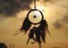 Shadowed dreamcatcher with feather tassels, a beautiful nod to traditions & customs, hangs against a sunset sky.