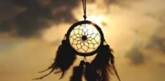 Shadowed dreamcatcher with feather tassels, a beautiful nod to traditions & customs, hangs against a sunset sky.