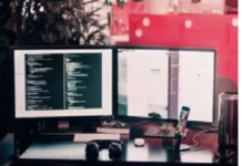 A dual monitor setup displays code on one screen and a chat or document on the other. A keyboard, mouse, headphones, and a smartphone are on the desk. Disruptive Technology