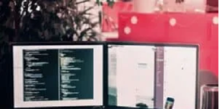 A dual monitor setup displays code on one screen and a chat or document on the other. A keyboard, mouse, headphones, and a smartphone are on the desk. Disruptive Technology