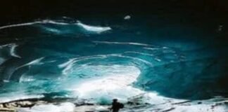 A person stands inside a large ice cave with illuminated blue walls and a rocky ground, feeling an odd sense of calm despite the potentially bad situation.