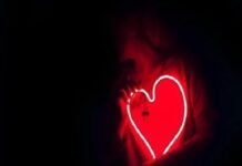 A person holds a glowing red neon heart-shaped sign, symbolizing vibrant health, against a dark background.