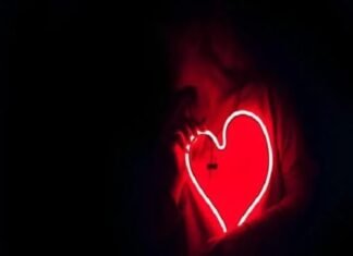 A person holds a glowing red neon heart-shaped sign, symbolizing vibrant health, against a dark background.