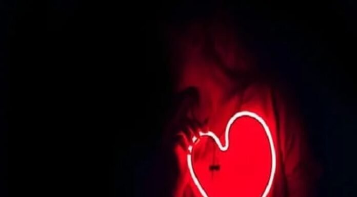 A person holds a glowing red neon heart-shaped sign, symbolizing vibrant health, against a dark background.