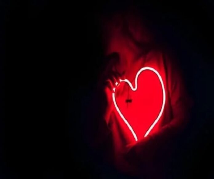 A person holds a glowing red neon heart-shaped sign, symbolizing vibrant health, against a dark background.