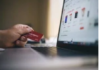 A person holds a red credit card, determined to get out of debt, while shopping online on a laptop displaying product listings.