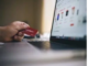 A person holds a red credit card, determined to get out of debt, while shopping online on a laptop displaying product listings.