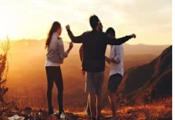 Four people stand on a hilltop at sunset, arms raised, overlooking a scenic view. How does your life shape your age