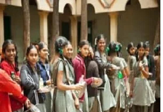 A group of middle class school students in uniform stands in a line outdoors, holding items in their hands, with trees and a building in the background.