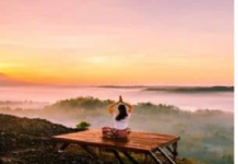 Person meditating on a wooden platform overlooking a misty valley at sunrise, finding peace of mind amidst the serene beauty.