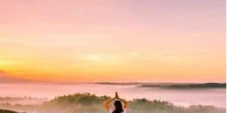 Person meditating on a wooden platform overlooking a misty valley at sunrise, finding peace of mind amidst the serene beauty.