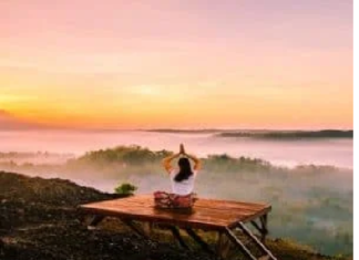 Person meditating on a wooden platform overlooking a misty valley at sunrise, finding peace of mind amidst the serene beauty.