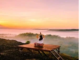 Person meditating on a wooden platform overlooking a misty valley at sunrise, finding peace of mind amidst the serene beauty.