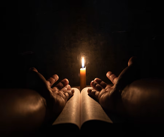 Hands holding a book with a candle symbolizing the power of God in the dark.