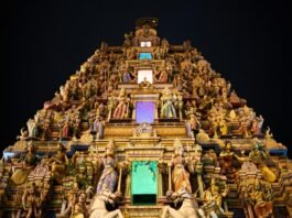An ornate Hindu temple is lit up at night, attracting visitors on their temple visits.