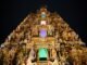 An ornate Hindu temple is lit up at night, attracting visitors on their temple visits.