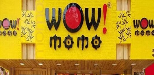 Front entrance of "Wow! Momo" restaurant with bright yellow signage and a staff member visible at the counter inside.