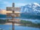 A wooden sign with "Mind," "Body," "Connection" stands gracefully against a serene lake and mountain backdrop, capturing the essence of natural health.