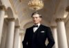 A man in a formal suit stands in an opulent hall with a chandelier and tall white columns, exuding both wealth and power reminiscent of John D. Rockefeller era.