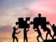 Silhouettes of people working together to fit giant puzzle pieces against a sunset background, embodying the spirit of challenges and personality development.