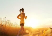 A person on running on a path through a field at sunset, embracing well-being in an orange top and shorts.