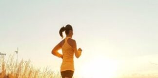 A person on running on a path through a field at sunset, embracing well-being in an orange top and shorts.