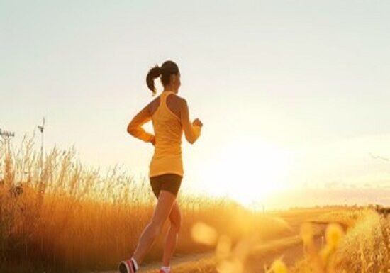 A person on running on a path through a field at sunset, embracing well-being in an orange top and shorts.