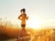 A person on running on a path through a field at sunset, embracing well-being in an orange top and shorts.