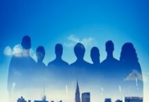 Silhouettes of seven people, representing teamwork, overlay a city skyline under a blue sky with clouds.