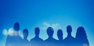 Silhouettes of seven people, representing teamwork, overlay a city skyline under a blue sky with clouds.