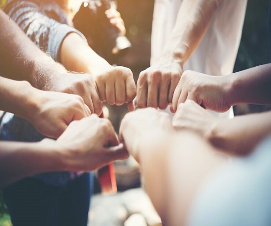 A group of people form a circle, each extending one fist towards the center, symbolizing teamwork in a unified gesture.