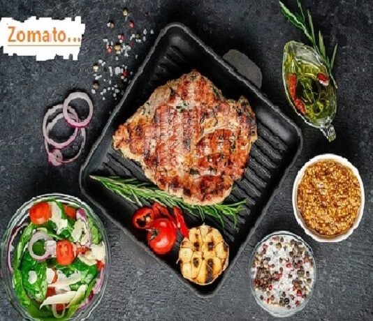 Grilled steak sizzles in a pan, paired with a vibrant side salad, roasted garlic, and condiments on a dark surface. A nod to "Zomato success story," the "Zomato" text graces the corner as a reminder of their culinary journey.