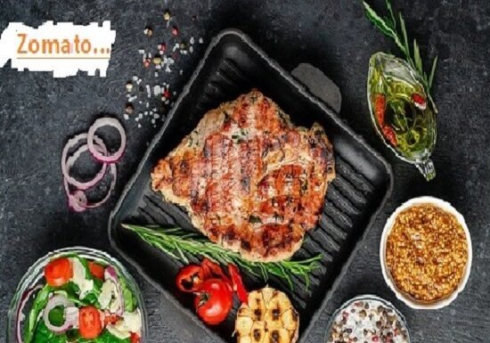 Grilled steak sizzles in a pan, paired with a vibrant side salad, roasted garlic, and condiments on a dark surface. A nod to "Zomato success story," the "Zomato" text graces the corner as a reminder of their culinary journey.