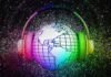 A globe with grid lines is encircled by headphones. The image is surrounded by a colorful, glittery background. The world is listening.