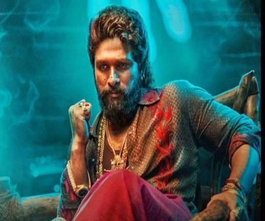 Allu Arjun with a beard and styled hair sits confidently in a colourful shirt and red pants, wearing multiple necklaces, resembling a icon star. The background features a blue-green glow.