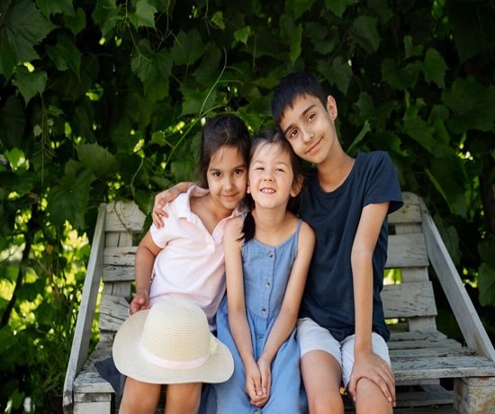 Three-child policy, nestled on a wooden bench surrounded by lush greenery, create a picturesque scene. The child on the left holds a straw hat, adding charm to their serene setting.