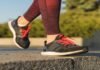 A person in red patterned leggings strides confidently on a stone surface, sporting black and red sneakers, perhaps the best running shoes for flat feet.