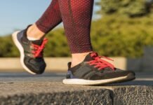 A person in red patterned leggings strides confidently on a stone surface, sporting black and red sneakers, perhaps the best running shoes for flat feet.