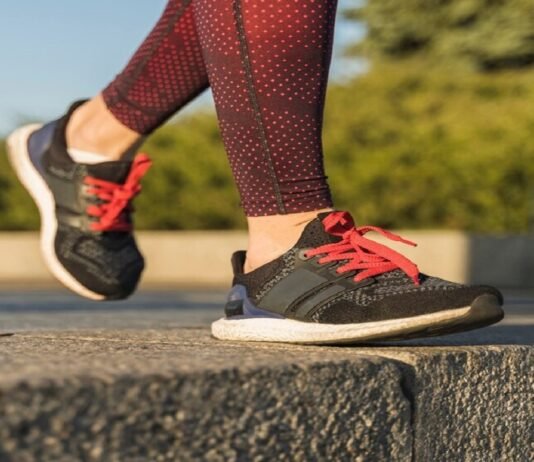 A person in red patterned leggings strides confidently on a stone surface, sporting black and red sneakers, perhaps the best running shoes for flat feet.