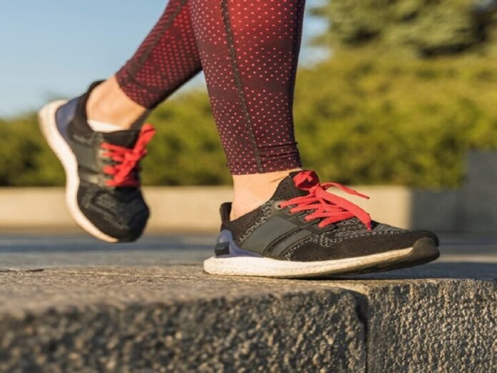 A person in red patterned leggings strides confidently on a stone surface, sporting black and red sneakers, perhaps the best running shoes for flat feet.