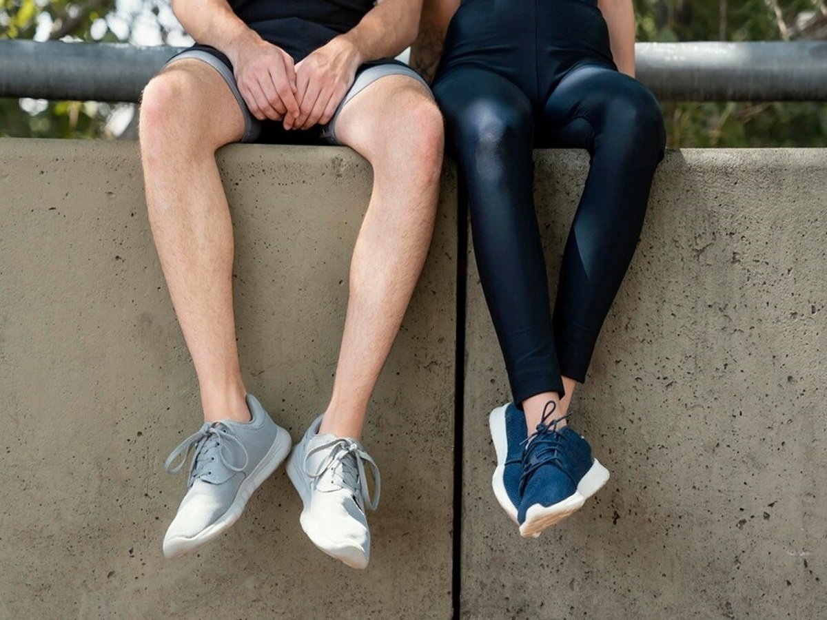 Two people sit on a concrete ledge, showing only their legs. One wears light gray sneakers and shorts; the other opts for dark blue sneakers and black leggings, both perfect choices for those seeking the best shoes for flat feet.