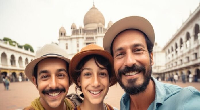 Three Indian immigrants wearing hats smile for a selfie in front of a historic building with domes and arches.