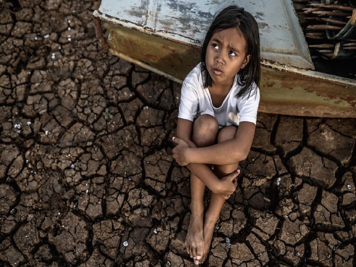 An Indian water crisis faced the child, who sat on dry, cracked earth, leaning against an old boat, looking thoughtful.